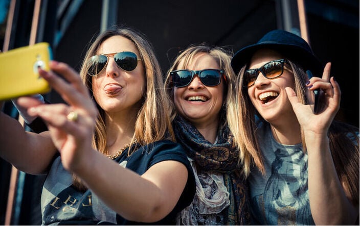 Three friends in sunglasses smiling for a group selfie